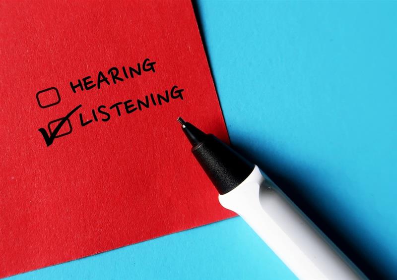 White pen on a blue background with a red sheet of paper, on it it is written hearing and listening with two check boxes and listening is checked