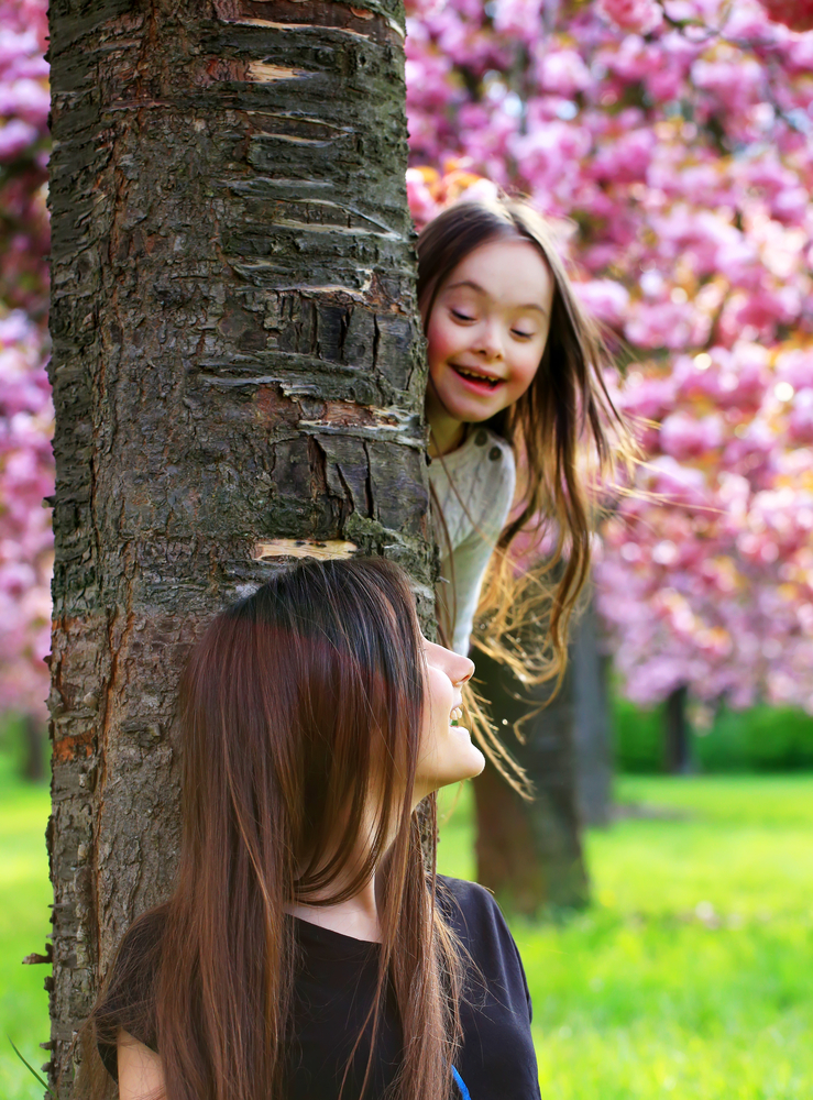 Girl and older woman playing hide and seek with blossom in the background