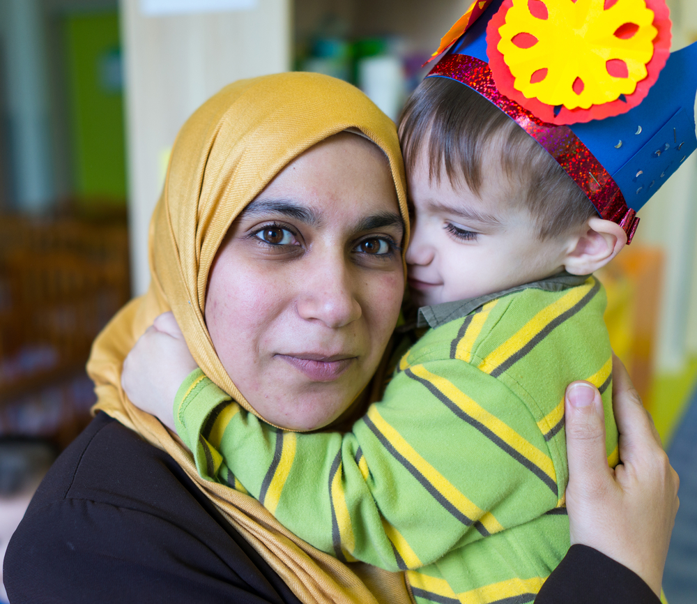 A woman wearing a green hijab smiling and holding a young boy, who is wearing a paper crown.
