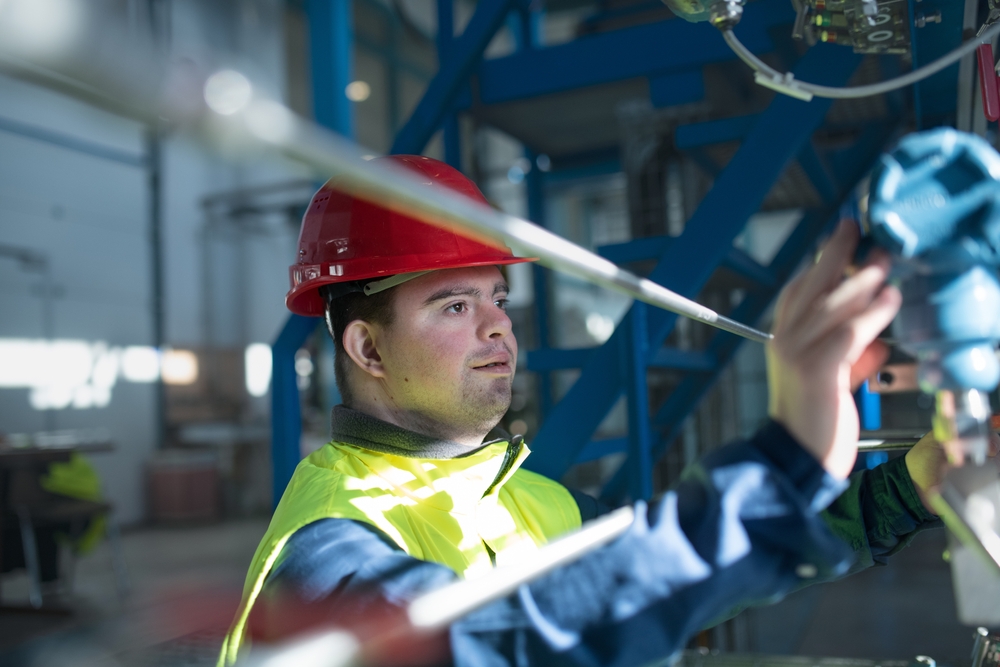 Smiling young man wearing a red hard hat and a hi-viz tabard operating a machine in a factory