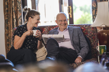 A man and his daughter having a cup of tea on the sofa