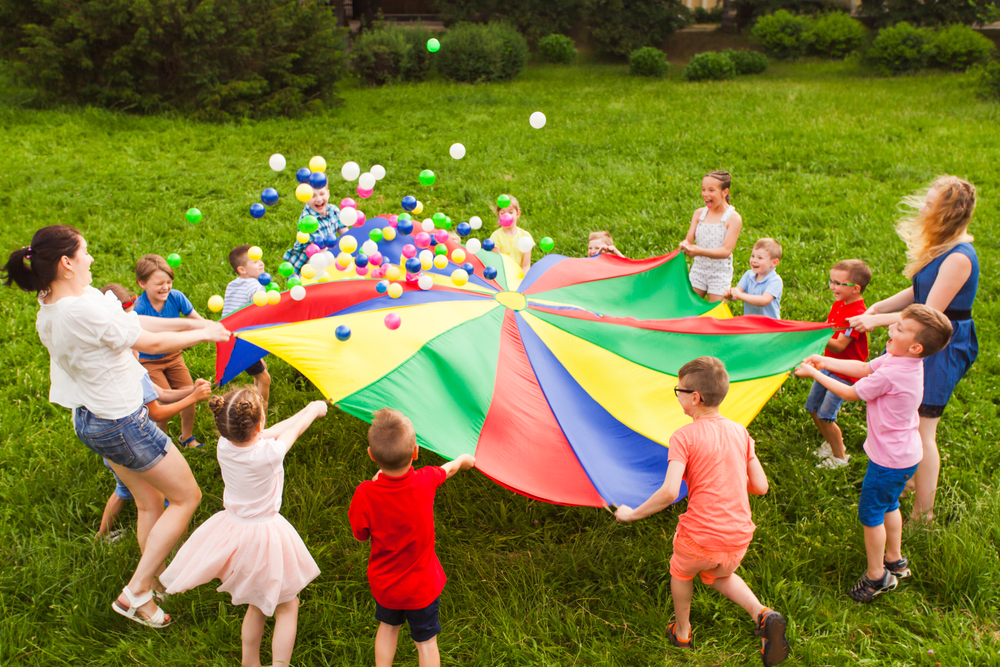 children playing outside with a parachute silk and balls