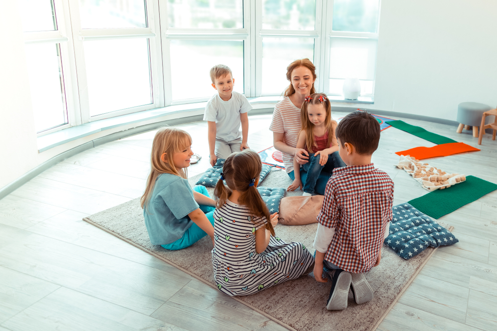 Five children aged 6-7 sitting  together with their teacher while sharing stories with 