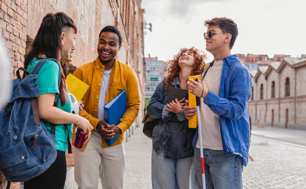 Four happy university students talking together on a city street, enjoying their time on campus. 