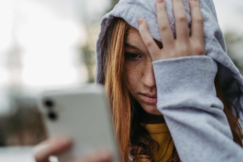 teen looks at her phone with sad expression