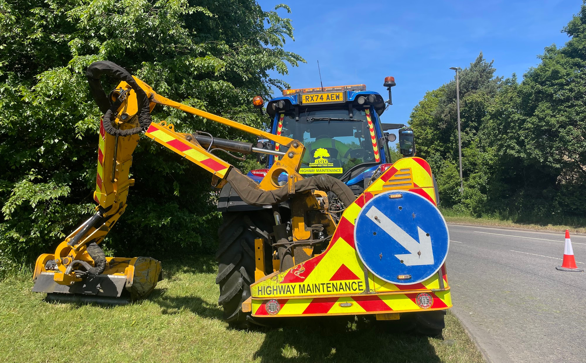 Photo of a highways maintenance tractor cutting a grass verge on a sunny day.