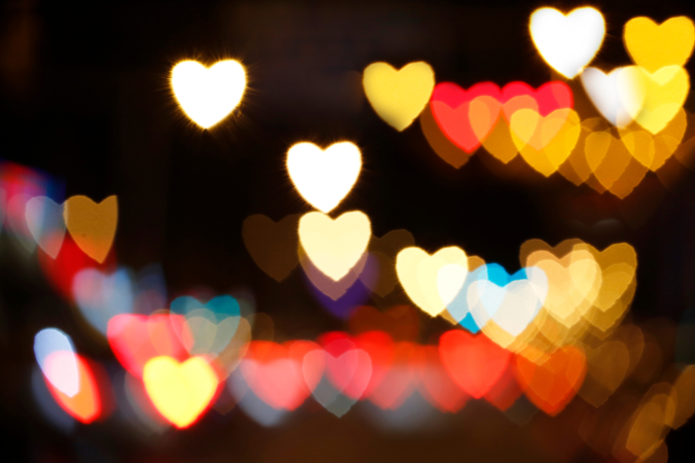 Crowd of multi-coloured heart-shaped lights in soft focus on a dark background.