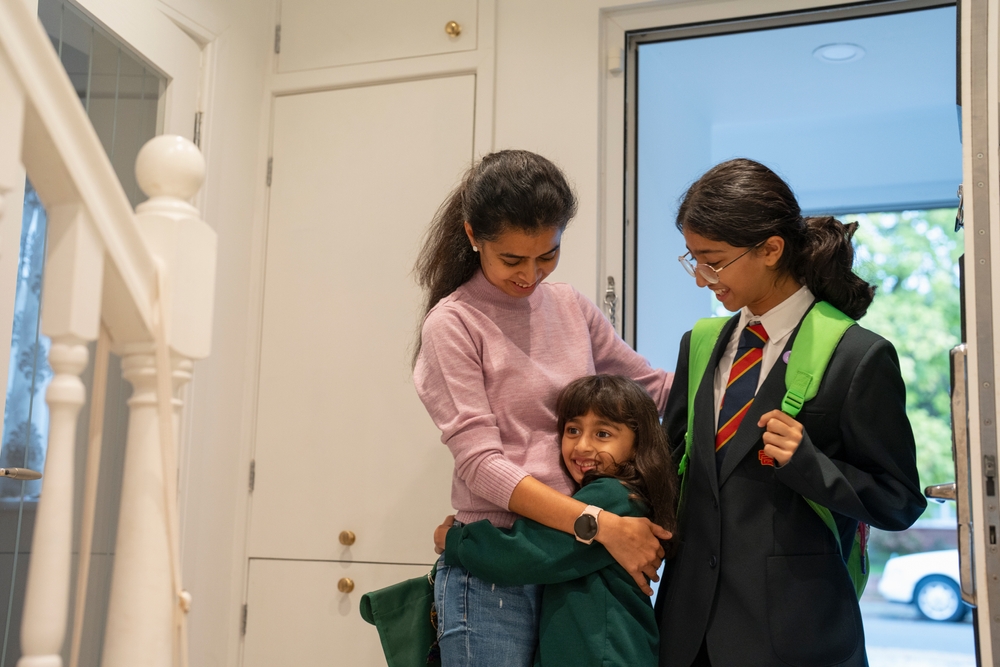 Two girls arrive home from school in uniform and embrace their mum 