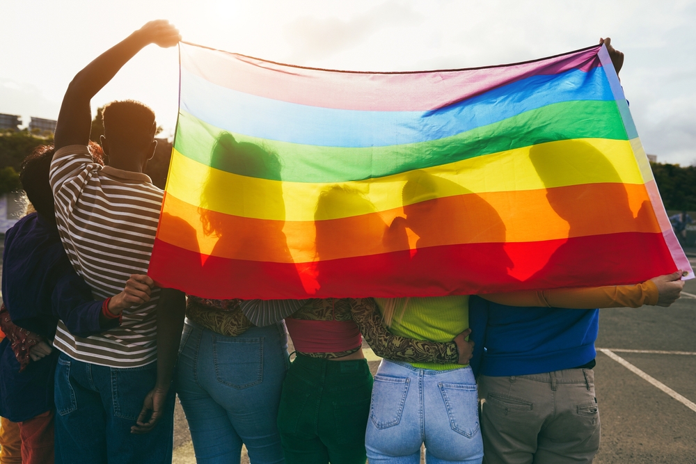 Five young people hold a Pride Flag in the sunshine 