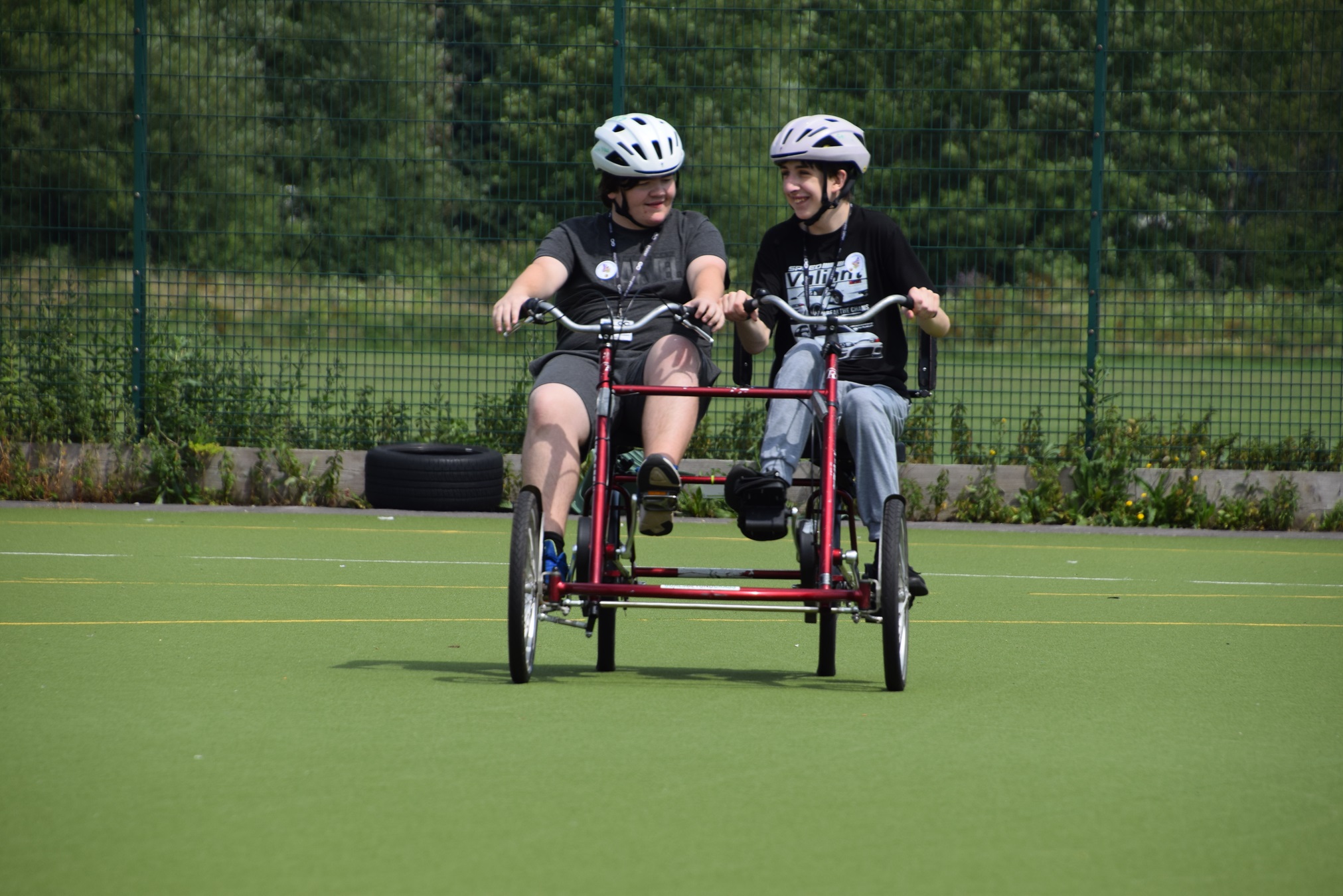 Two young people enjoy a ride together on an adapted bike on the turf at Oxstalls campus.  