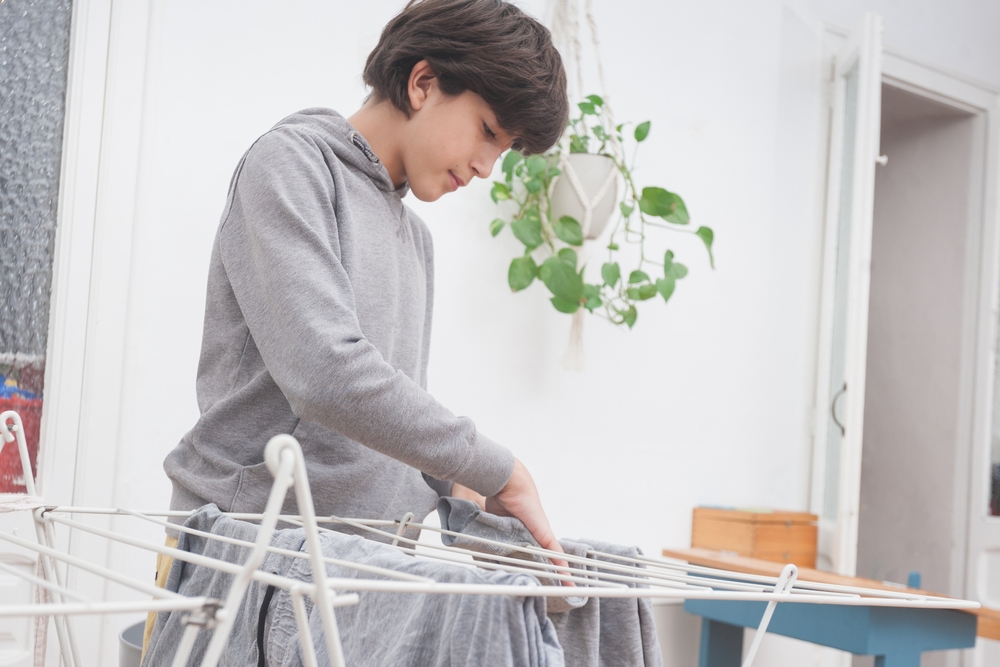14 year-old using a clothes airer on which to hang washing in a conservatory