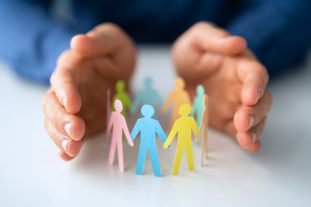 Pair of human hands around paper cut out of people holding hands